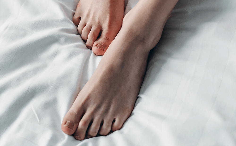 Close up of feet while woman lies on white bed