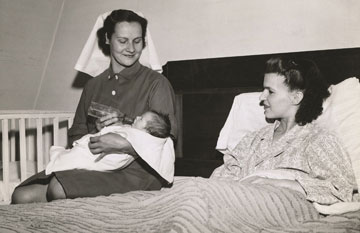 Black and white photo of VHA staff feeding a child beside a mother in bed