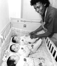 Black and white photo of a VHA employee and 3 babies in a crib