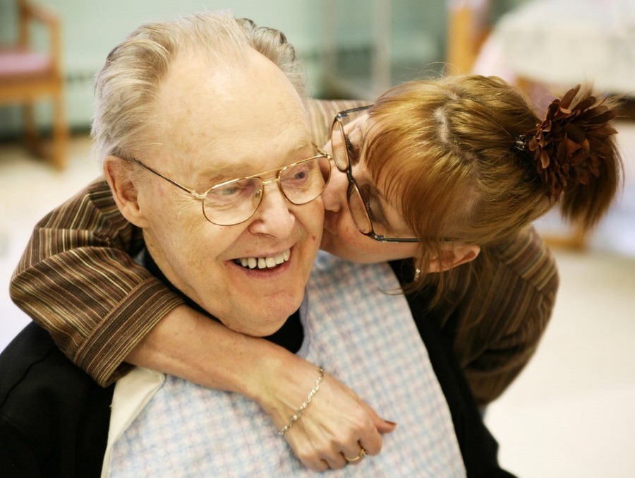 Daughter gives her elderly father a kiss on the cheek while hugging him