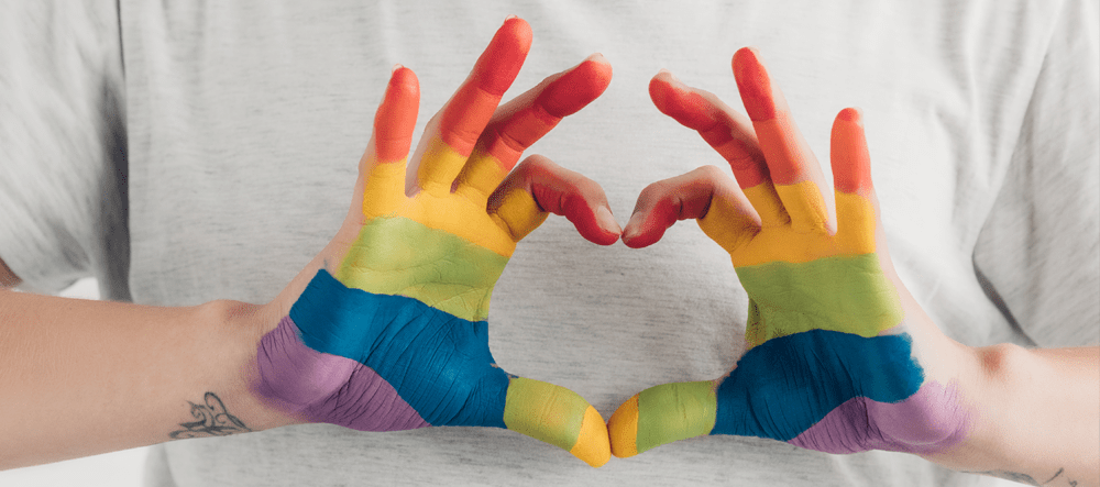 Rainbow painted hands make a heart shape to celebrate Pride
