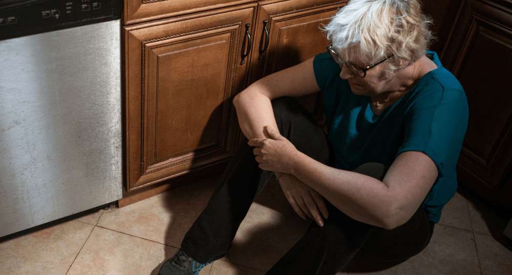 Depressed elderly women seated on kitchen floor beside dishwasher