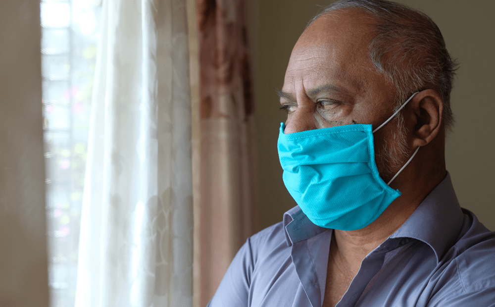 Senior man looking out window while wearing mask