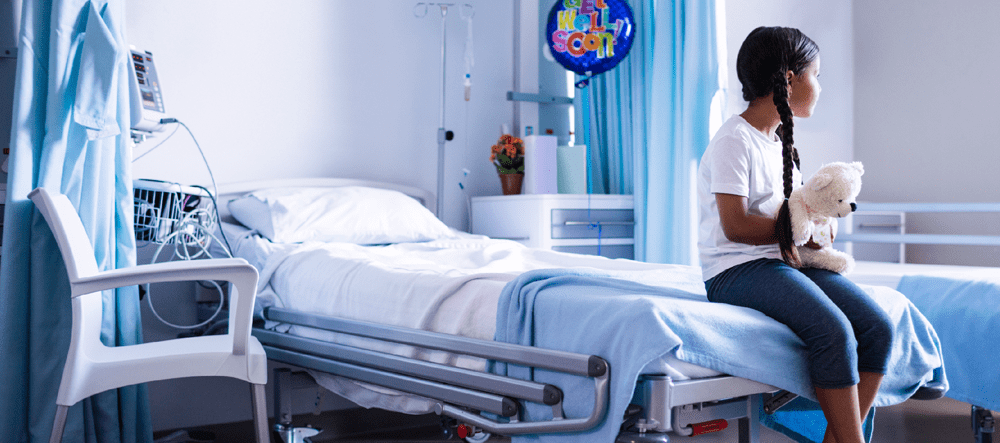 Young girl sitting at the end of a hospital bed