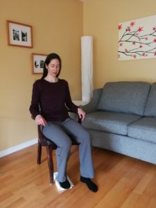 Woman sitting on a chair with one foot positioned behind the other