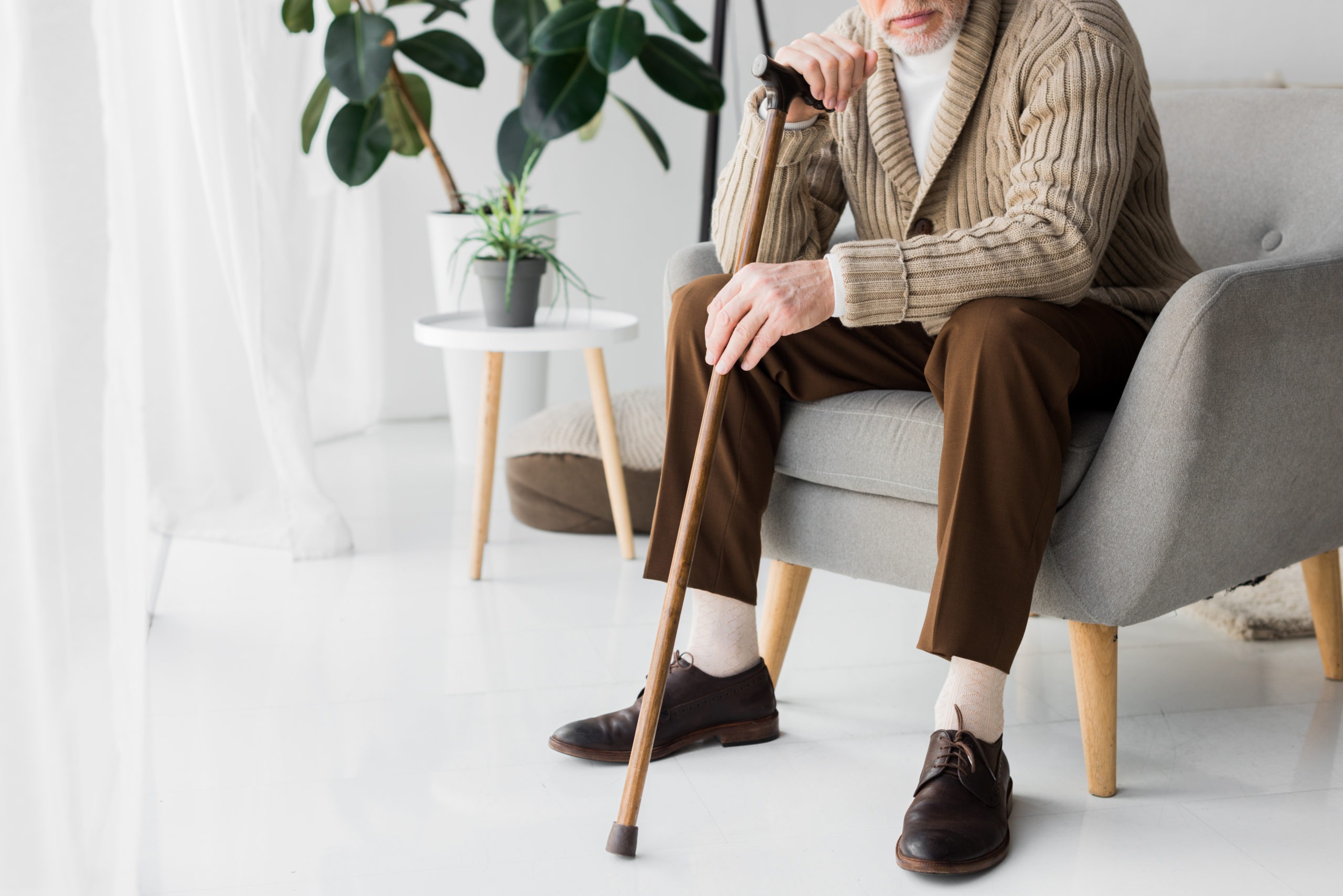 A stylish senior sits in a chair leaning forward onto his cane
