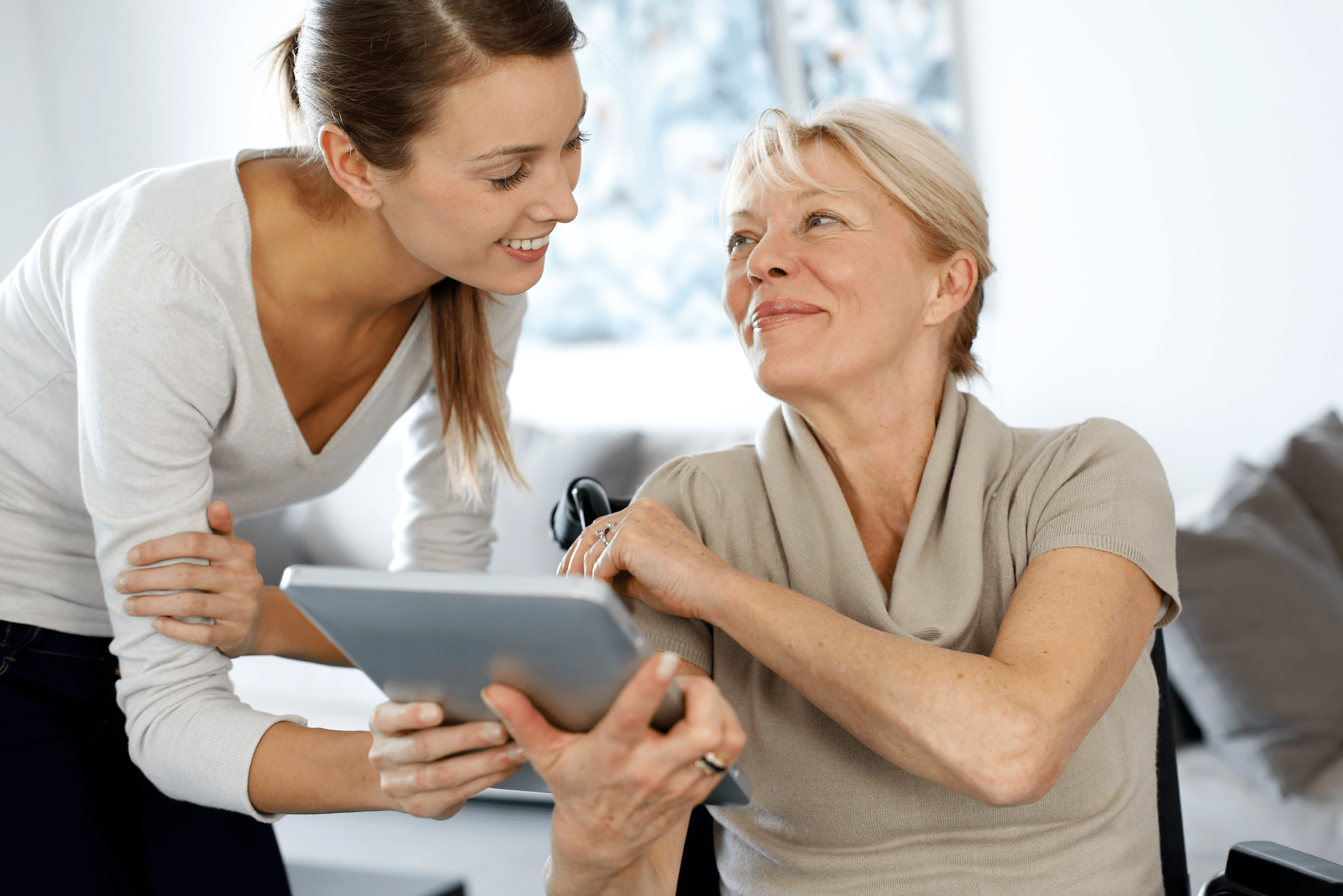 Girl showing tablet to elderly woman in wheelchair