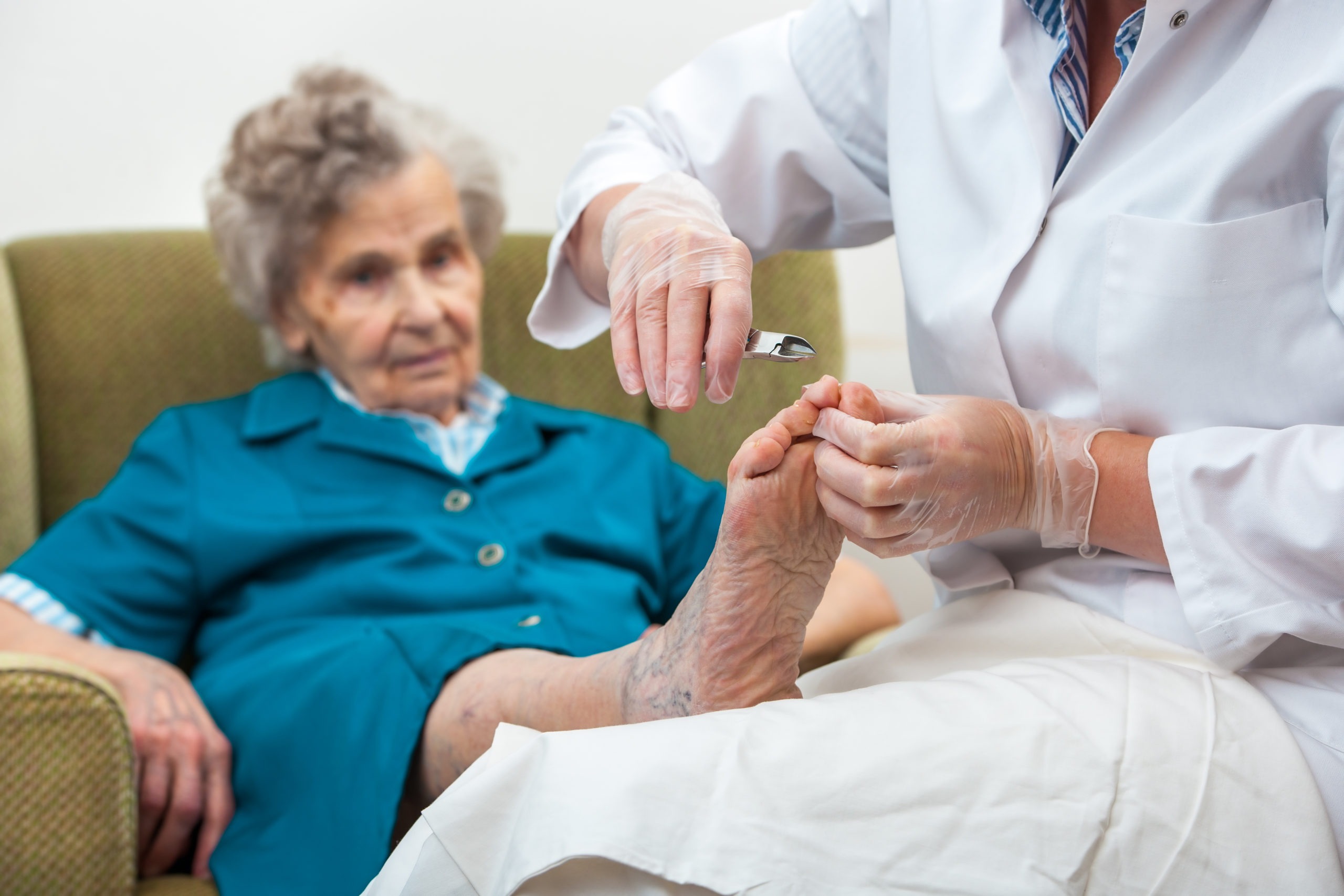 Nurse assists an elderly woman with chiropody and body care at home
