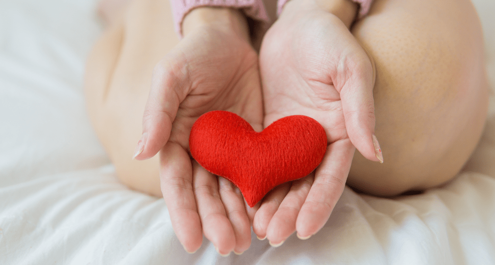 Women sitting on bed and holding a felt heart in her hands