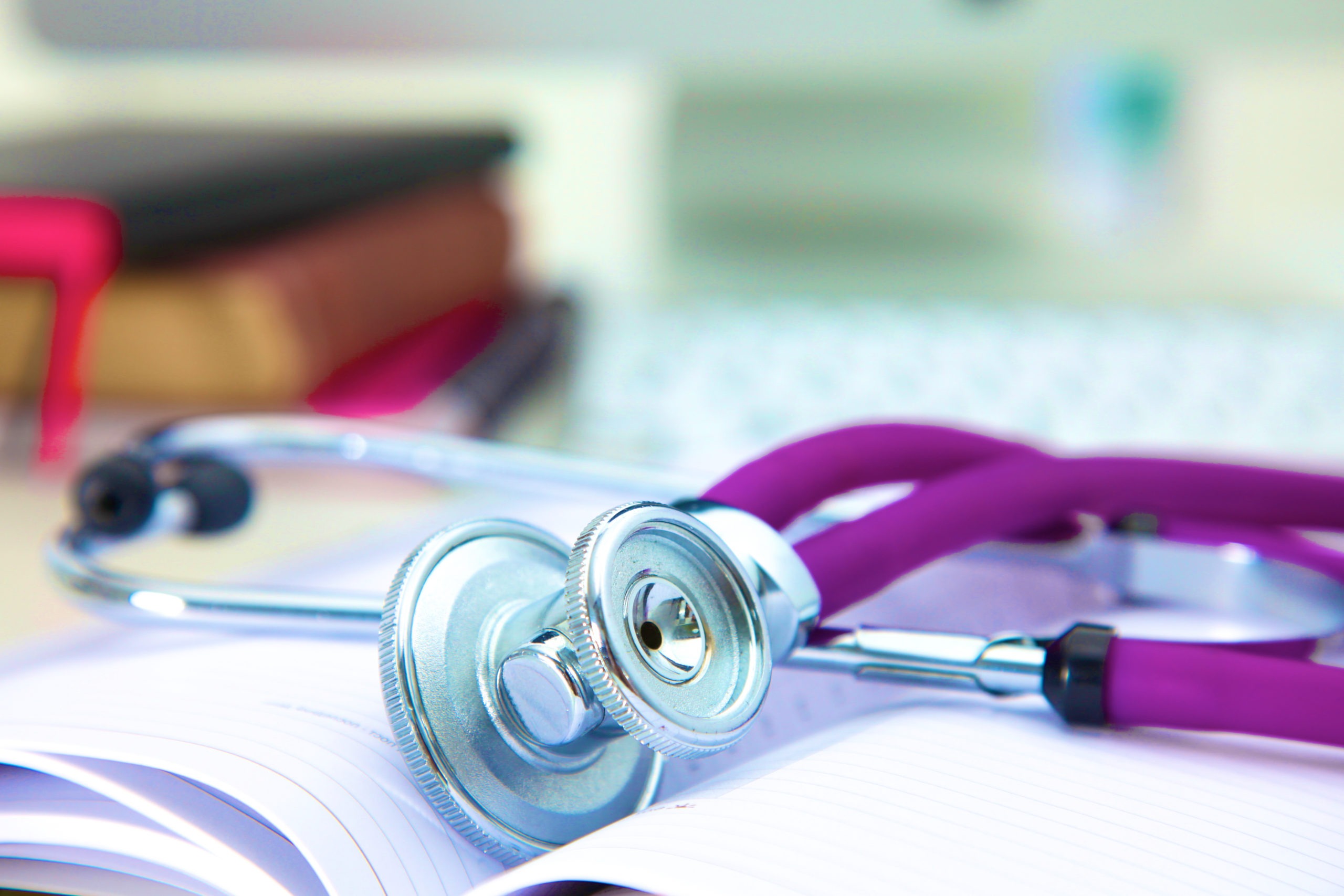 Medical stethoscope with old books and laptop on a table.