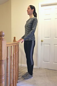 Physiotherapist stands at a stair railing with her feet together while demonstrating the Feet Together balance exercise