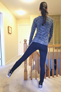 Physiotherapist stands and holds a stair railing one leg raise to her left side while demonstrating the Side Leg Raise balance exercise