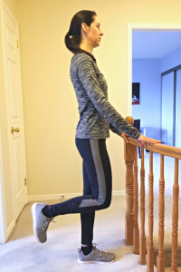 Physiotherapist stands and holds a stair railing with one leg raised behind her while demonstrating the Single Leg Stance balance exercise