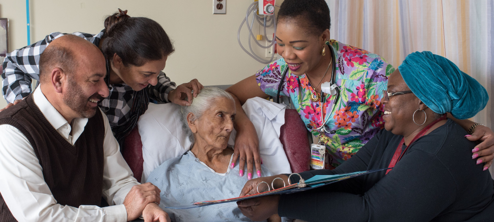 A family and care providers around a patient in a hospital bed.