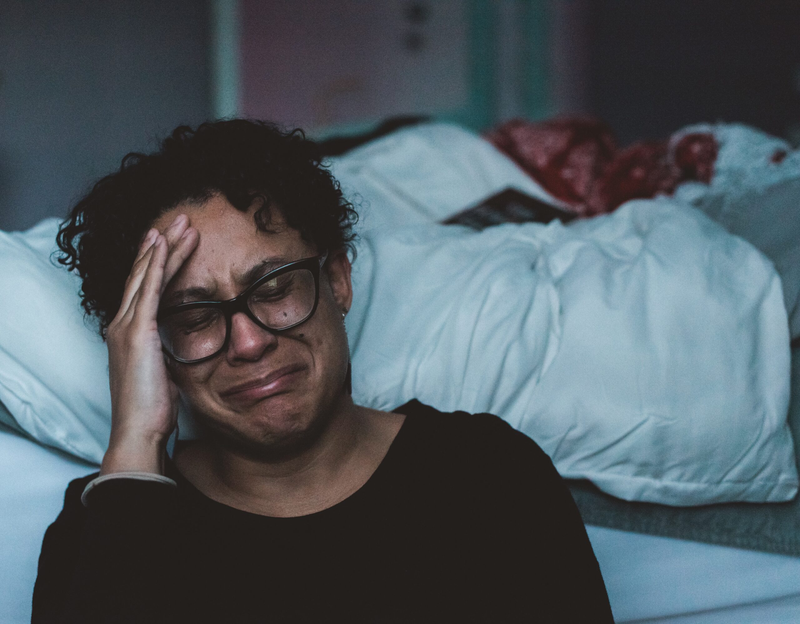 Woman holding head and crying next to bed