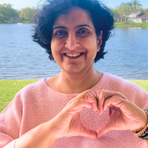 Board member Karen poses in front of a lake, her hands in the shape of a heart.