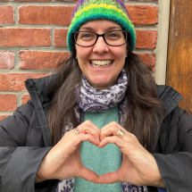 Case worker Lucie poses in front of brick wall, her hands in the shape of a heart.