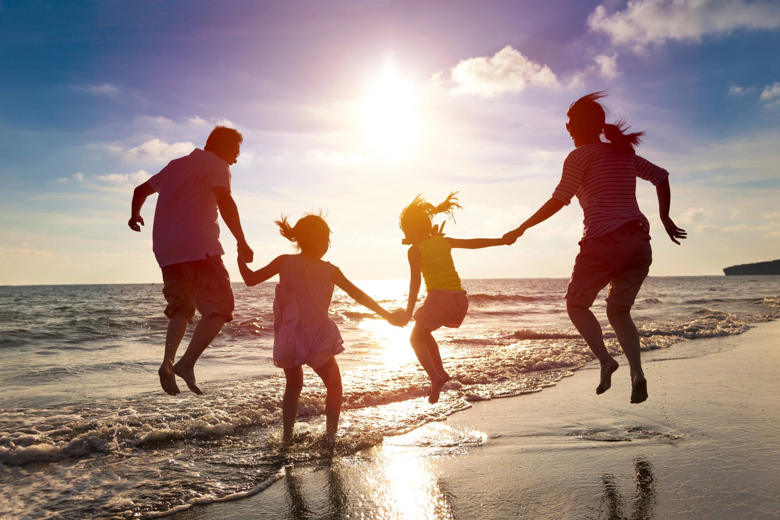 Family on the beach, holding hands and jumping with the sun setting