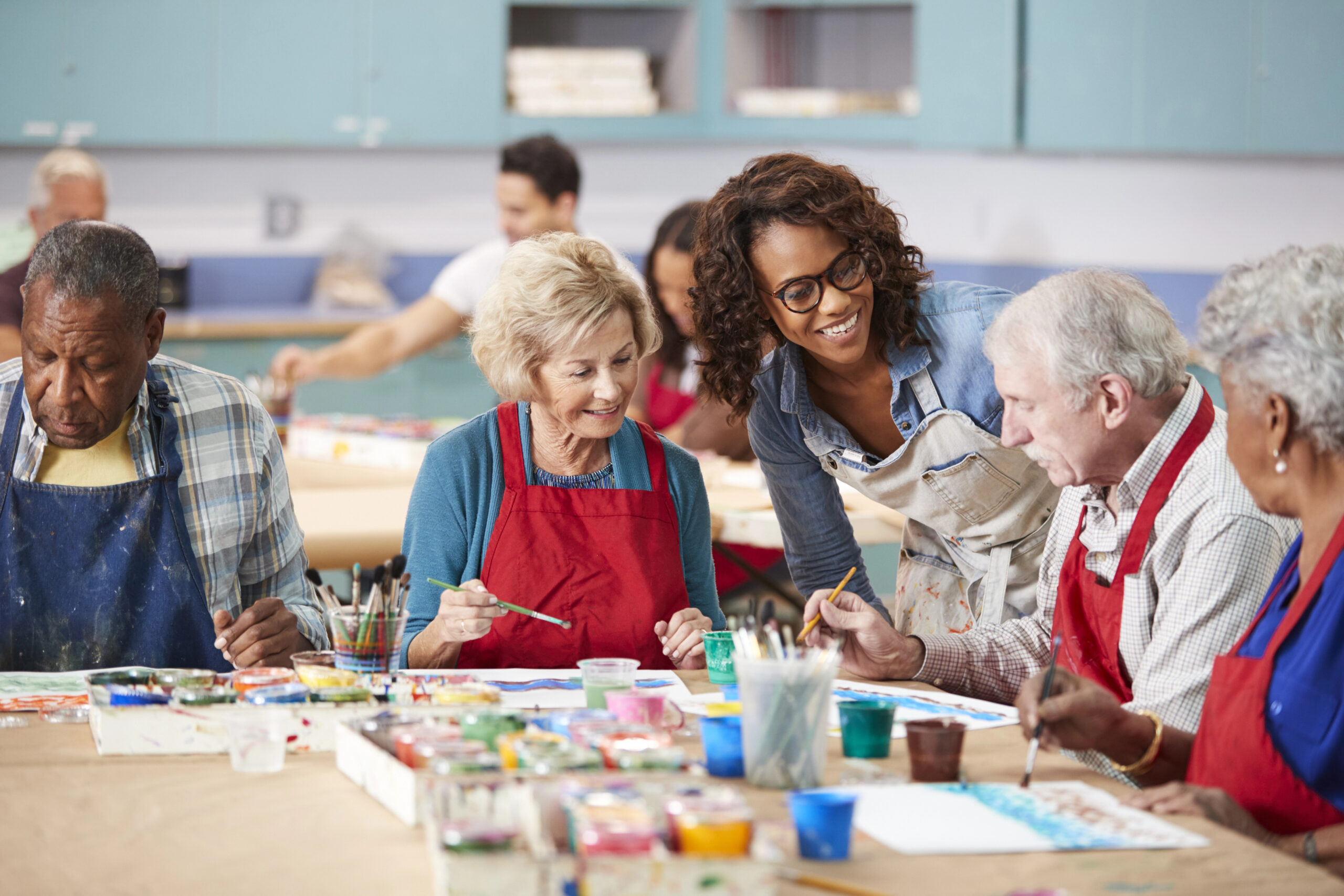 Group of older adults painting together in an art class with a teacher.