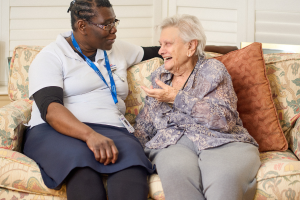 A personal support worker and female, senior client sitting on a couch together talking