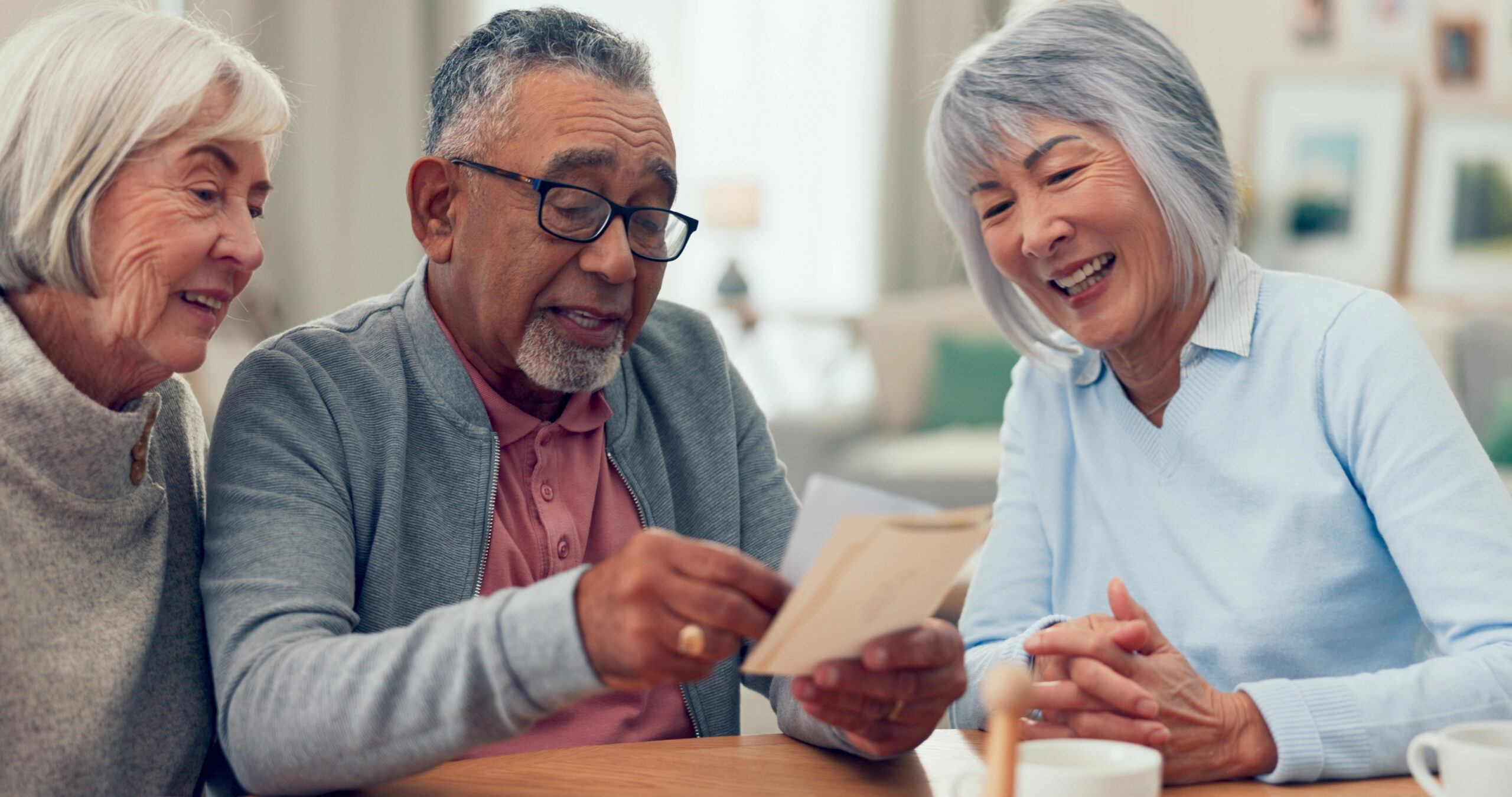Three older adults sitting together at a table, looking at photos and smiling.