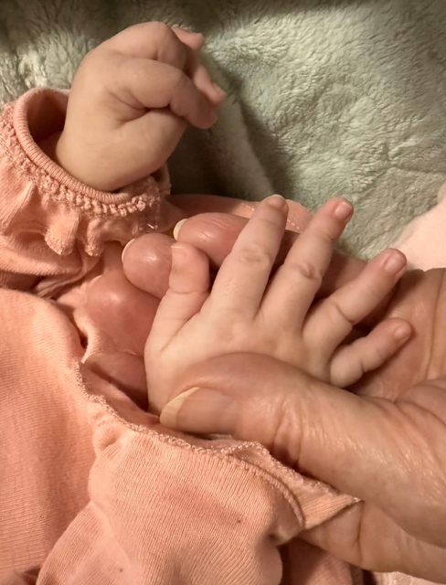 An adult holding a baby's hand.