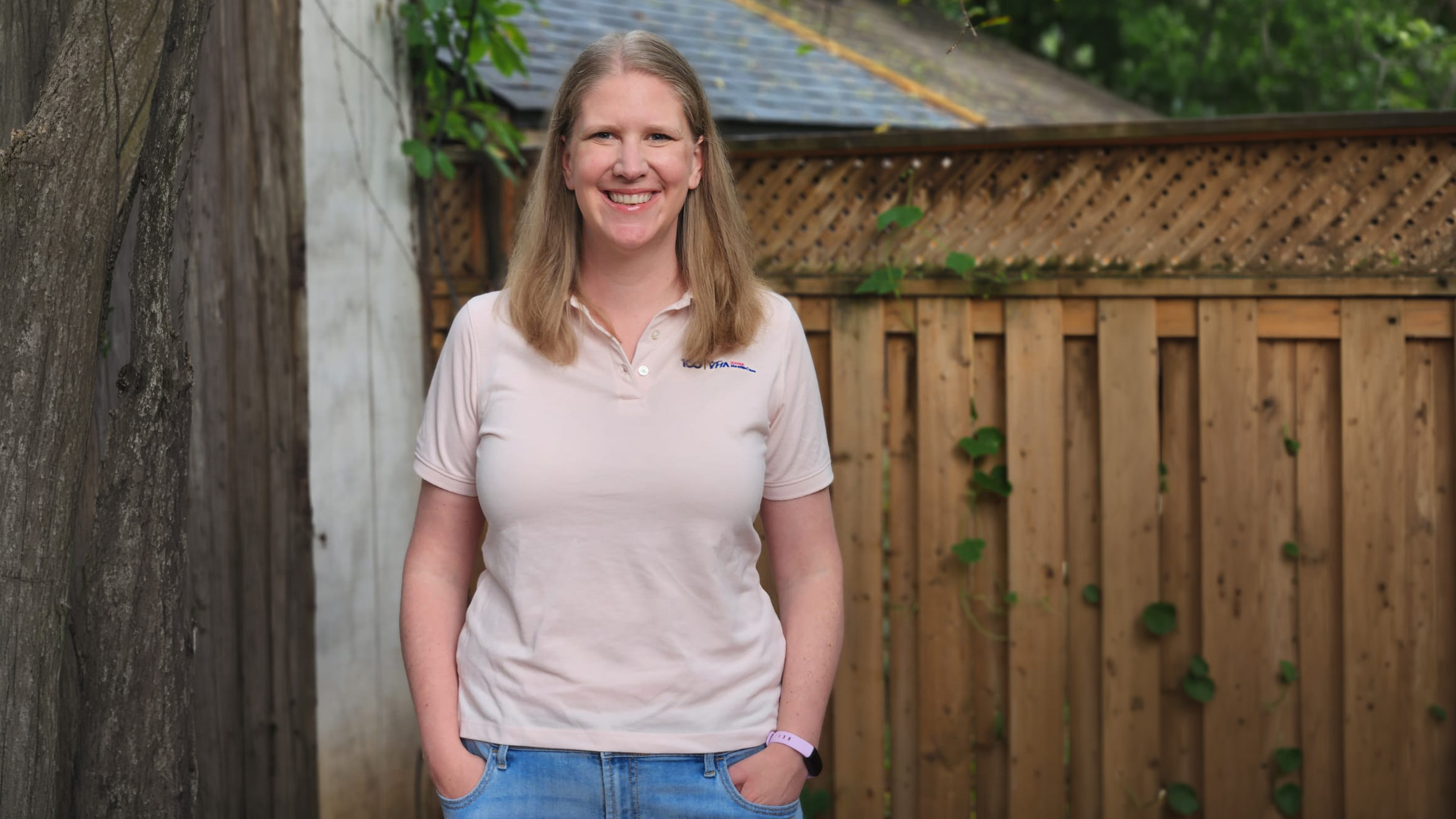 Volunteer Jenn Barios standing and smiling in a backyard, in front of a fence.